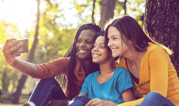 Three smiling people taking a picture under a tree